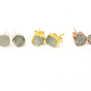 May include: Three pairs of earrings with raw, light blue gemstone stones. The earrings are set in silver, gold, and rose gold.