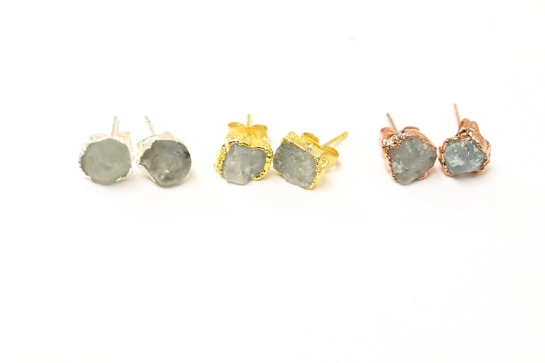 May include: Three pairs of earrings with raw, light blue gemstone stones. The earrings are set in silver, gold, and rose gold.