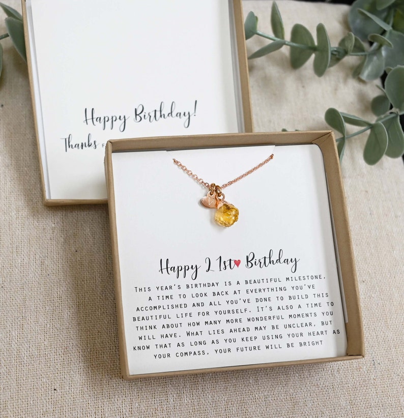 May include: A gift box with a necklace inside. The necklace has a small heart charm and a larger, orange gemstone charm. The box has a card inside that reads "Happy 21st Birthday." This year's birthday is a beautiful milestone. A time to look back at everything you've accomplished and all you've done to build this beautiful life for yourself. It's also a time to think about how many more wonderful moments you will have. What lies ahead may be unclear, but know that as long as you keep using your heart as your compass, your future will be bright.