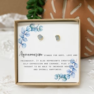 May include: A small box with a pair of aquamarine earrings. The box has a watercolor design of eucalyptus leaves and the text "Aquamarine STANDS FOR HOPE, LOVE AND FRIENDSHIP. IT ALSO REPRESENTS CREATIVITY, SELF-EXPRESSION AND COURAGE, PLUS IT'S THOUGHT TO BE ABLE TO INCREASE HEALTH AND OVERALL HAPPINESS."