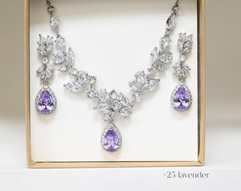 May include: A silver necklace and earrings set with a delicate leaf design and purple teardrop crystals. The set is displayed in a white box with the text "#25 lavender" on the bottom.