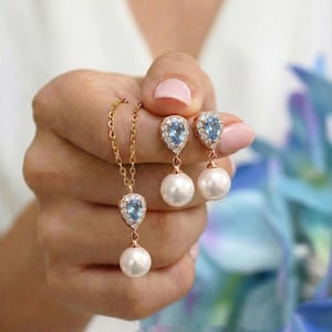 May include: A gold-colored necklace and earrings set. The necklace has a teardrop-shaped blue gemstone pendant with a white pearl. The earrings have a similar design. The text "#8 blue as shown" is at the bottom.
