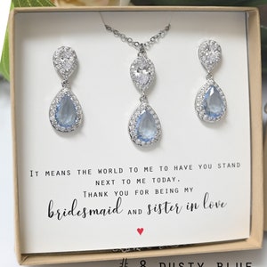 May include: A gift box containing a silver necklace and earrings with teardrop-shaped blue stones. The box has a card that reads "It means the world to me to have you stand next to me today. Thank you for being my bridesmaid and sister in love."  #8 DUSTY BLUE