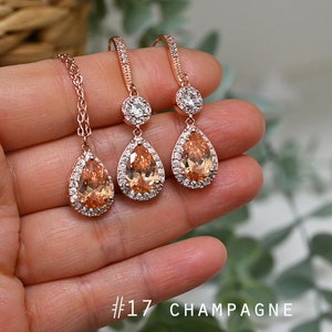 May include: Rose gold bridal jewellery set with a teardrop shaped pendant necklace and matching earrings. The stones are champagne coloured and have a clear crystal halo.