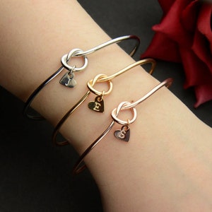 May include: Three gold knot bracelets with heart charms. Each charm has a different initial, J, E, and S.