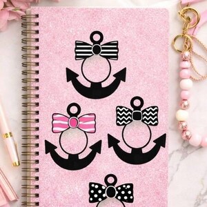 Pode incluir: Caderno rosa com espiral e textura brilhante, com desenhos de &acirc;ncoras pretas com la&ccedil;os estampados. Os la&ccedil;os t&ecirc;m listras, ziguezagues e bolinhas. Uma caneta e flores rosas est&atilde;o no fundo.