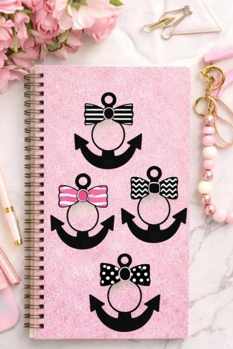 Pode incluir: Caderno rosa com espiral e textura brilhante, com desenhos de &acirc;ncoras pretas com la&ccedil;os estampados. Os la&ccedil;os t&ecirc;m listras, ziguezagues e bolinhas. Uma caneta e flores rosas est&atilde;o no fundo.