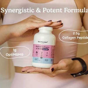 May include: A white bottle of Zen Principle Marine Collagen & MSM OptiMSM is held in front of a person. The bottle has a pink and blue label. Text on the image reads "Synergistic & Potent Formula", "1g OptiMSM", and "2.5g Collagen Peptides".