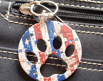 May include: A round, paw-shaped keychain with a patriotic design. The keychain features red and blue stripes with white stars, resembling the American flag. It is attached to a silver metal ring.