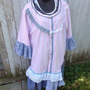 May include: A pink and blue striped shirt with lace trim and floral fabric accents. The shirt has a button-up front and is styled as a tunic or dress.