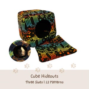 May include: A black fleece cube hideout for small pets featuring a colorful pattern of rainbows, stars, and clouds. The set includes a matching square floor mat and a circular inset showing a guinea pig inside a similar patterned hideout.