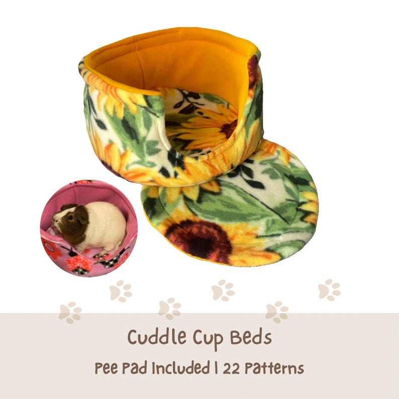 May include: A soft, round pet bed featuring a sunflower print on a white background with a solid yellow interior lining. A separate circular matching pad is included. A small inset shows a brown and white guinea pig resting in a pink floral bed.