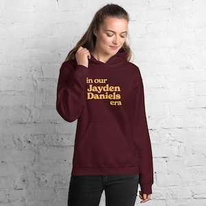 May include: Burgundy hoodie with a gold print that says "in our Jayden Daniels era".