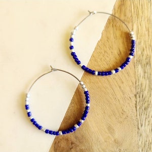 May include: A pair of silver hoop earrings with blue and silver beads. The earrings are on a wooden surface.