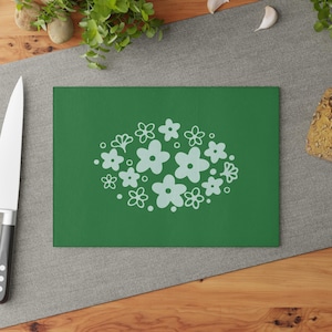 May include: A rectangular, green cutting board with a cluster of light blue flowers in the center. The flowers are in various sizes and shapes. A stainless steel knife is on the left side of the board.