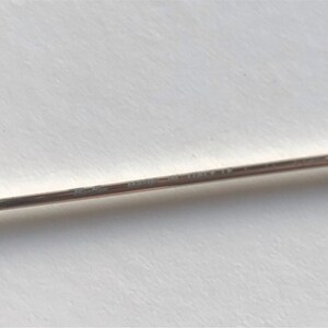 Puede incluir: Primer plano de un objeto delgado de metal plateado con el texto "Cartier" y "MADE IN ITALY CE" grabado. El objeto est&aacute; sobre un fondo blanco.