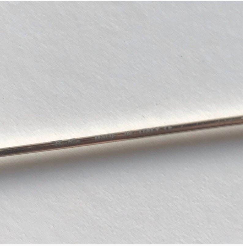 Puede incluir: Primer plano de un objeto delgado de metal plateado con el texto "Cartier" y "MADE IN ITALY CE" grabado. El objeto est&aacute; sobre un fondo blanco.