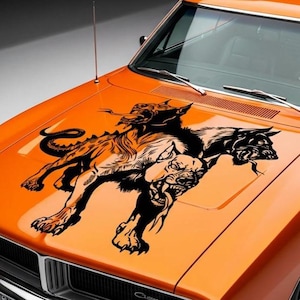 May include: An orange car hood with a black and tan graphic of a three-headed dog. The illustration depicts a snarling, mythical beast with sharp teeth and a long, serpentine tail. The car's hood is glossy and reflects the surrounding environment.