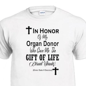 May include: White t-shirt with black text: "IN HONOR Of My Organ Donor Who Gave Me The GIFT OF LIFE Eternal Thanks!" with cross symbols. The Gildan brand shirt is a tribute to organ donors.