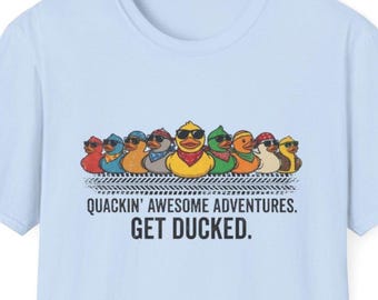 May include: Pale blue t-shirt with a graphic of cartoon ducks in sunglasses and bandanas. The text reads "QUACKIN' AWESOME ADVENTURES. GET DUCKED." The shirt is made of a soft fabric, suitable for casual wear.