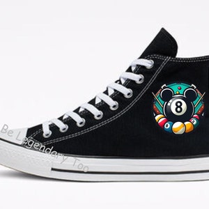 以下が含まれることがあります： 白いソールと、緑色のフェルトのビリヤード台に8の数字とミッキーマウスの耳が付いたビリヤードボールのカラフルなグラフィックが描かれた、黒いハイカットキャンバススニーカーです。