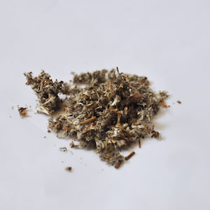 May include: A pile of dried, shredded plant material, with a mix of brown, gray, and white hues. The texture appears fibrous and slightly coarse, suggesting it may be used for herbal remedies or crafts. The background is plain white.
