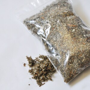 May include: A clear plastic bag filled with dried herbs, with a small pile of herbs next to the bag. The herbs are a mix of green, brown, and tan, and appear to be sage or a similar type of herb.