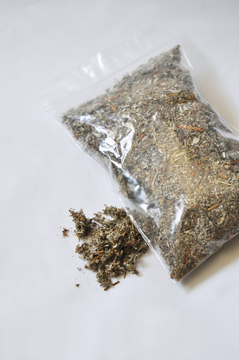 May include: A clear plastic bag filled with dried herbs, with a small pile of herbs next to the bag. The herbs are a mix of green, brown, and tan, and appear to be sage or a similar type of herb.