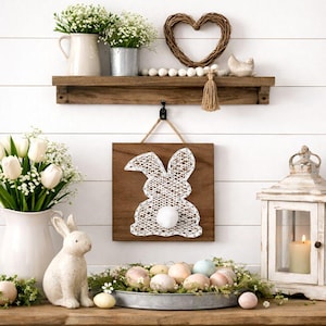 Op de afbeelding: Een rustieke paasdecoratie met een houten plank met bloemstukken, een hartvormige krans en een draadkunstkonijn. Een keramisch konijn en een dienblad met versierde eieren maken de lentedecoratie compleet.