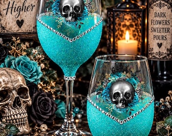 May include: Two clear glass vessels, one stemmed wine glass and one stemless tumbler, featuring a vibrant turquoise glitter base, a silver skull graphic surrounded by teal floral accents, and a decorative V-shaped rhinestone trim.