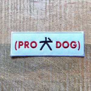 Peut inclure: Écusson rectangulaire blanc avec le texte brodé en rouge (PRO 大 DOG) sur un fond en bois.