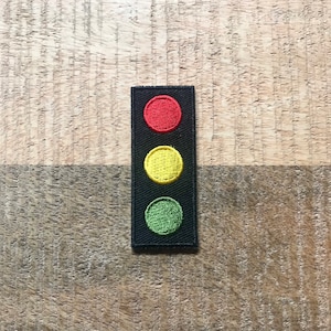 Puede incluir: Un parche de semáforo negro y rojo con una luz roja en la parte superior, una luz amarilla en el medio y una luz verde en la parte inferior.