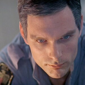 May include: A close-up of a man's face with a serious expression. He is wearing a blue shirt with a patch that says "United States Space Agency, Mission Discovery".