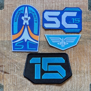以下が含まれることがあります： 青と白で「Mission Infinity」と「SC 15」の文字が書かれた刺繍パッチ4つ、白い羽根のシンボルが描かれた青いパッチ、幾何学模様の青い「15」が書かれた黒いパッチ