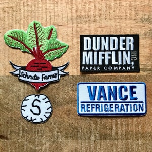 Puede incluir: Cuatro parches bordados, dos con texto blanco sobre fondo negro, uno con texto blanco sobre fondo azul y uno con texto blanco sobre fondo rojo. Los parches presentan el texto "Dunder Mifflin, Inc. Paper Company", "Vance Refrigeration", "Schrute Farms" y una "S" estilizada.