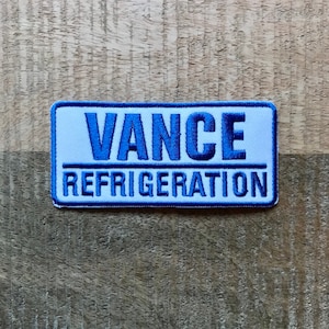 Puede incluir: Parche rectangular blanco con texto bordado en azul que dice "VANCE REFRIGERATION".