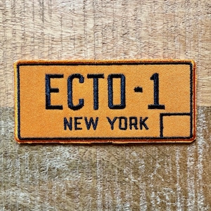 Puede incluir: Parche de tela naranja y negro con el texto "ECTO-1 NEW YORK" en negro.