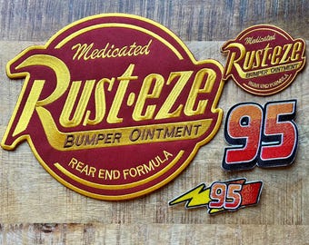 May include: A collection of embroidered patches featuring a large circular Rust-eze Medicated Bumper Ointment logo in maroon and yellow, a smaller circular Rust-eze logo, a large number 95 patch, and a small lightning bolt patch with the number 95.