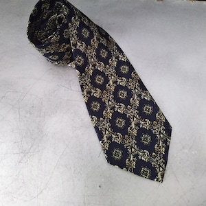 May include: A dark blue tie with a gold patterned design. The pattern features intricate swirls and floral motifs.