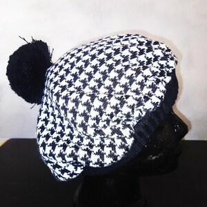 May include: Black and white houndstooth patterned knit beret with a black pom pom on top.
