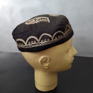 May include: A black embroidered cap with a gold design. The cap is on a mannequin head.