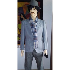Puede incluir: Un maniquí vestido con una blazer azul claro, pantalones grises y un sombrero fedora gris. Una bufanda a cuadros en azul, blanco y burdeos está drapeada alrededor del cuello. Guantes negros se sostienen en una mano. Estilo vintage clásico.