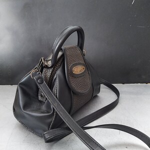 Puede incluir: Un bolso de mano de cuero negro con asa superior y una larga correa para el hombro. El bolso tiene un diseño texturizado y una hebilla dorada.