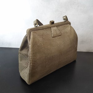 Könnte beinhalten: Eine beige Clutch aus Schlangenleder mit einem goldenen Verschluss und einem oberen Henkel.