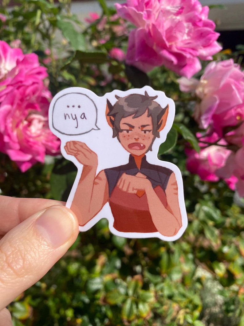 May include: A sticker featuring a cartoon character with pointed ears and a stern expression. The character is wearing a red and black outfit and has the word "nya" in a speech bubble. The sticker is held in front of a background of pink roses.