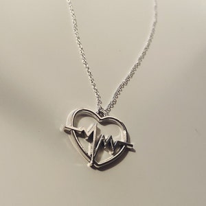May include: A silver necklace with a heart-shaped pendant featuring a stylized EKG line inside the heart.