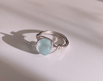 May include: A silver wire wrapped ring with a light blue oval-shaped gemstone.