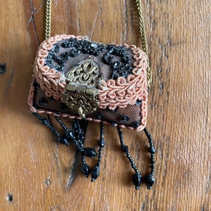 May include: A small, beaded, brown and pink purse with a gold chain and a gold clasp. The purse has black beads hanging from the bottom.
