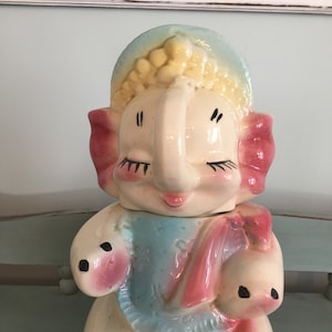 May include: A vintage ceramic elephant cookie jar with a blue and pink floral pattern. The elephant has a pink hat and pink ears. The jar is in good condition with some minor wear.