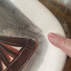 May include: A white ceramic plate with a brown and gray abstract design. The plate has a signature in the corner.